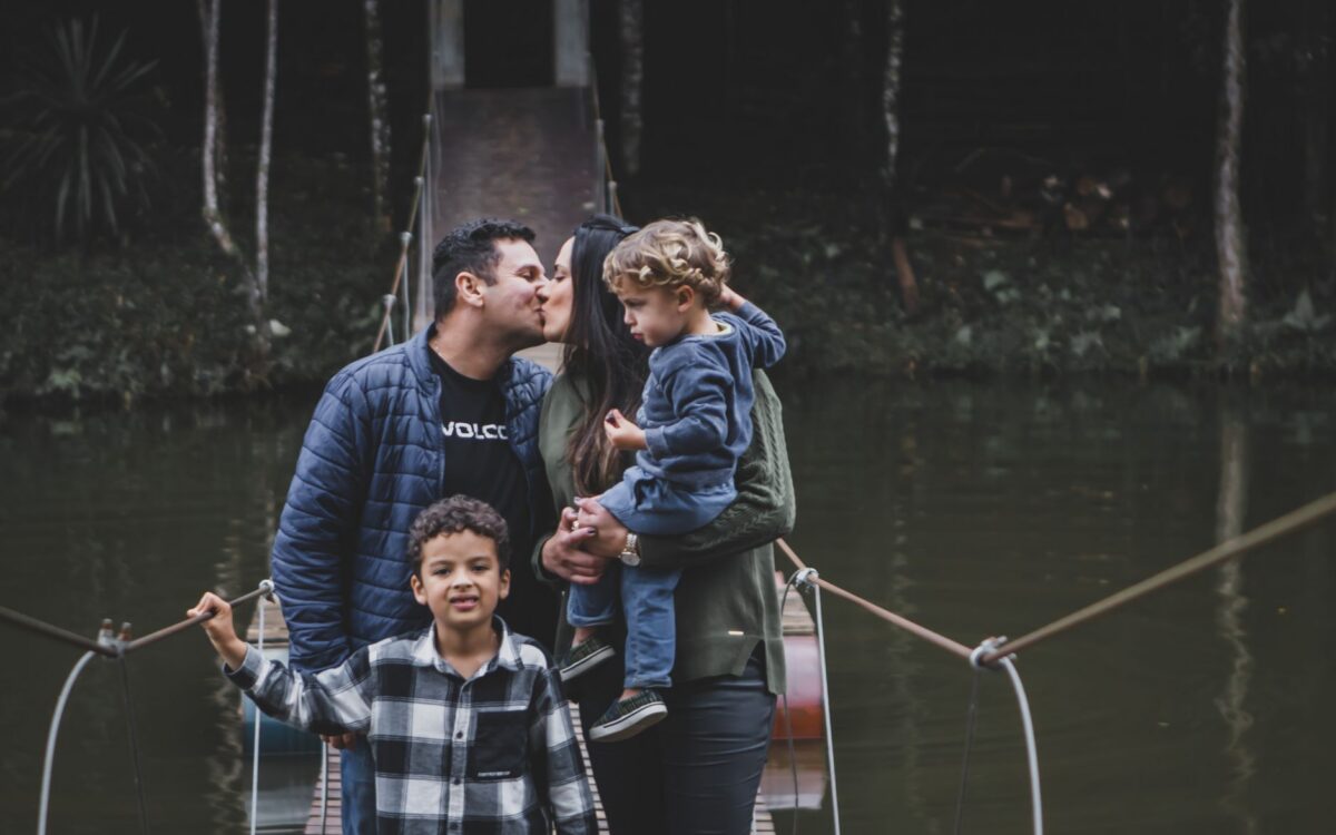Família se beijando em uma ponte suspensa cercada pela natureza