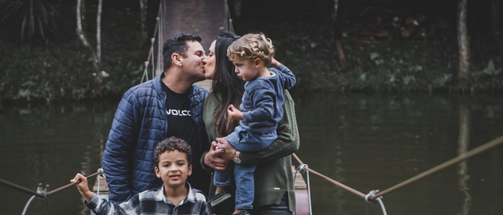Família se beijando em uma ponte suspensa cercada pela natureza