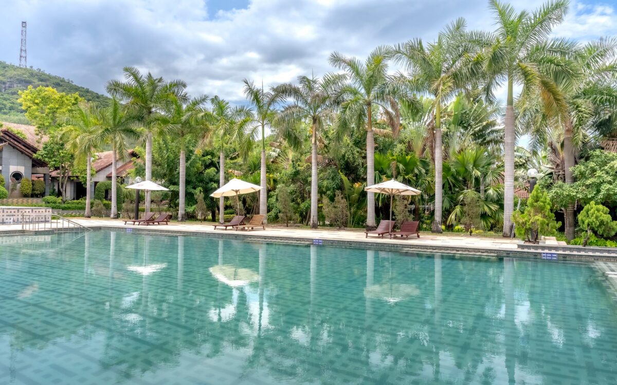 Vista serena à beira da piscina com palmeiras e espreguiçadeiras sob céus nublados