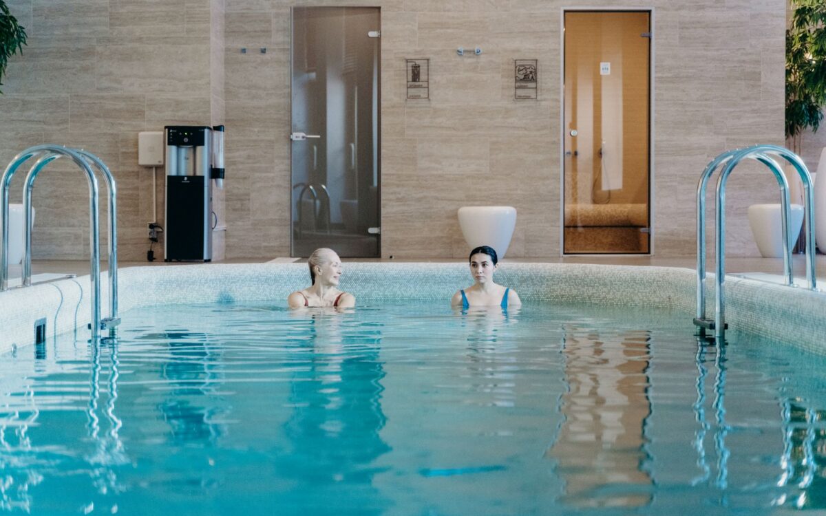 Duas mulheres desfrutando de um nado tranquilo em uma piscina coberta, capturando relaxamento e tranquilidade