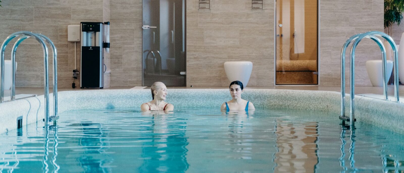 Duas mulheres desfrutando de um nado tranquilo em uma piscina coberta, capturando relaxamento e tranquilidade